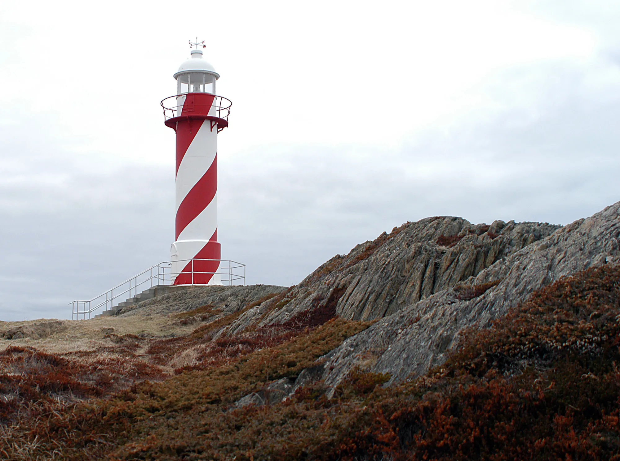 Red-and-white Heart's Content lighthouse on the rocks, overcast.