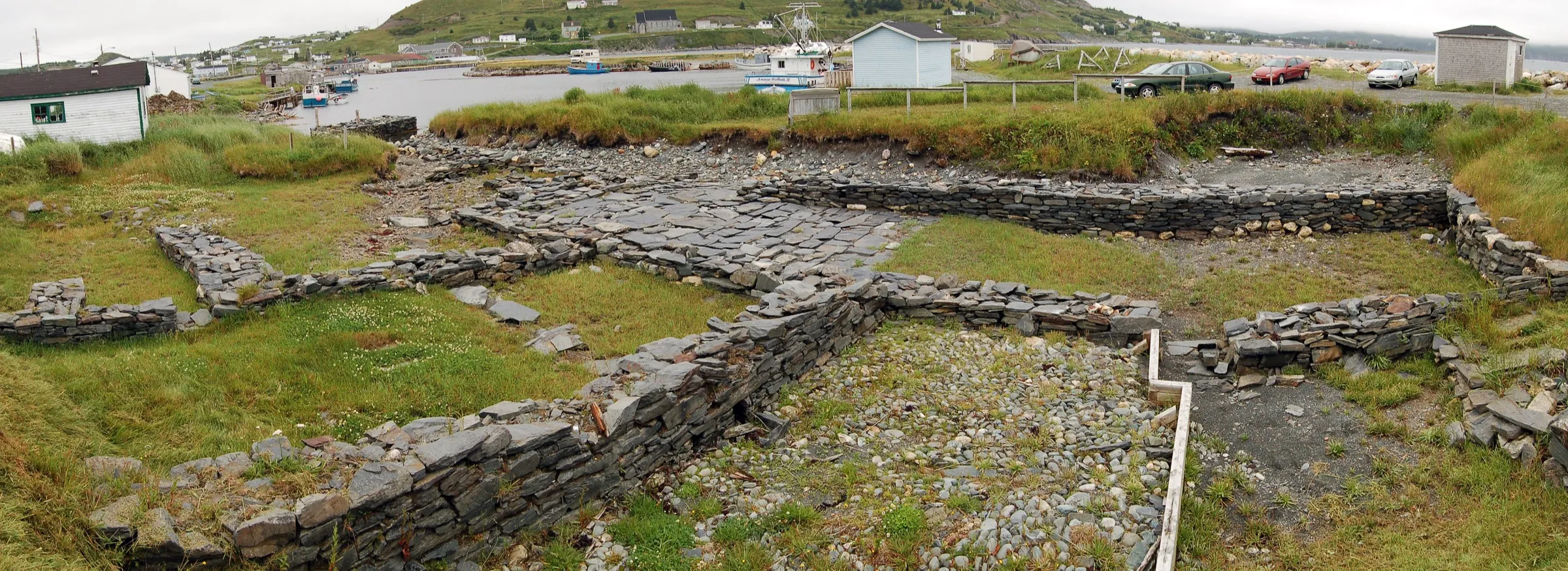 The excavated stone foundations of the 17th-century Colony of Avalon at Ferryland, laid out along the harbour with the village behind.