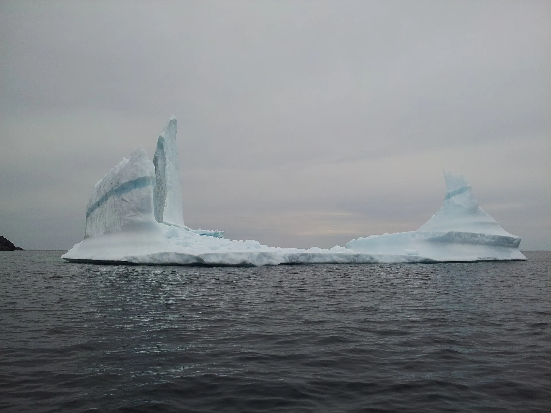A twin-pinnacled iceberg grounded off Exploits Island in Notre Dame Bay, photographed from a boat at water level.