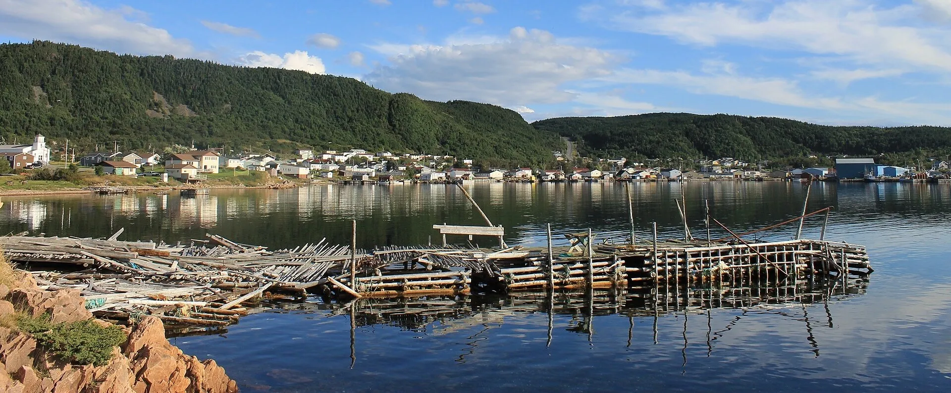 La Scie around its harbour at the top of the Baie Verte Peninsula — church, houses and fish flakes reflected in still water.
