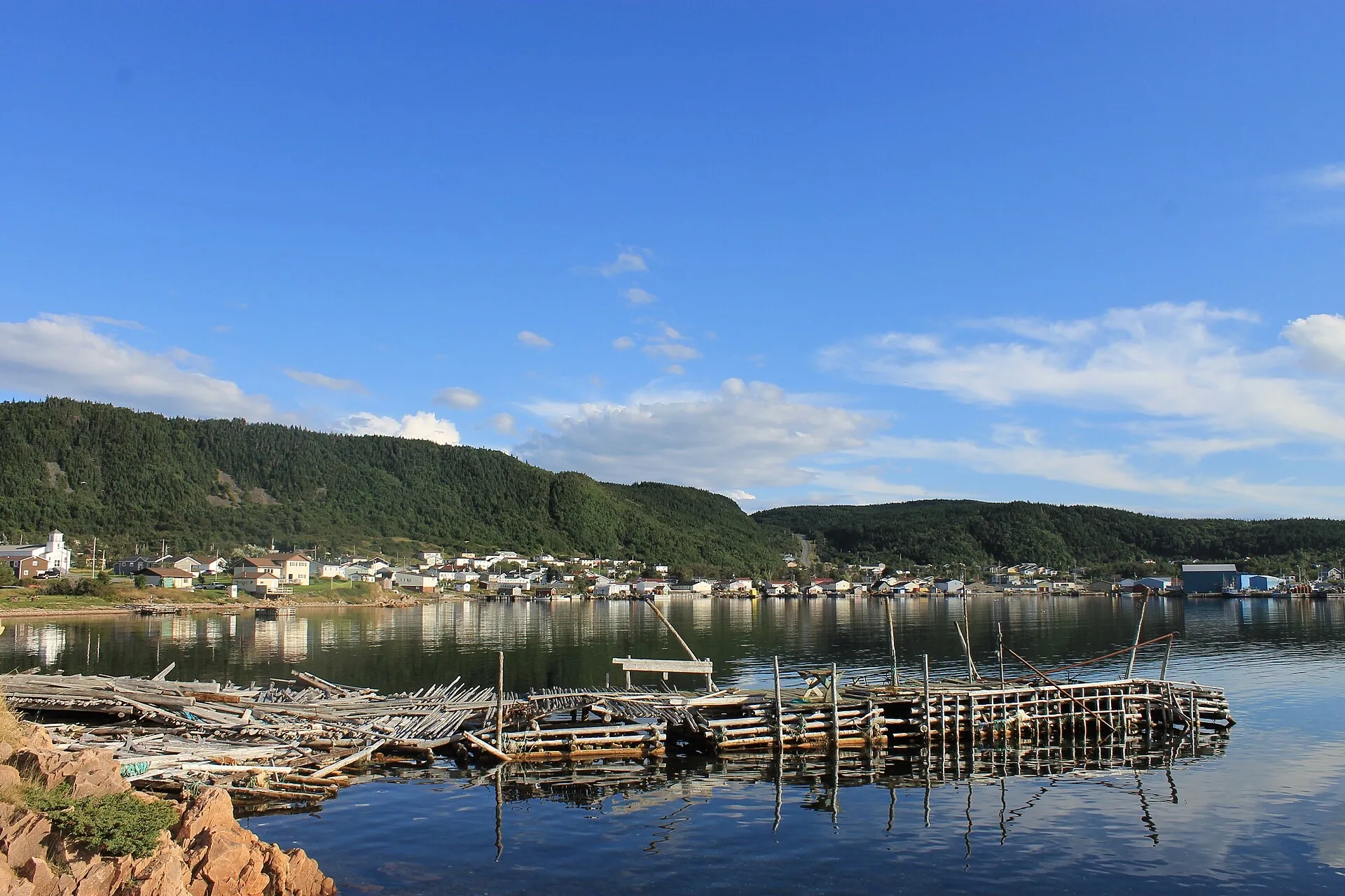 La Scie around its harbour at the top of the Baie Verte Peninsula — church, houses and fish flakes reflected in still water.
