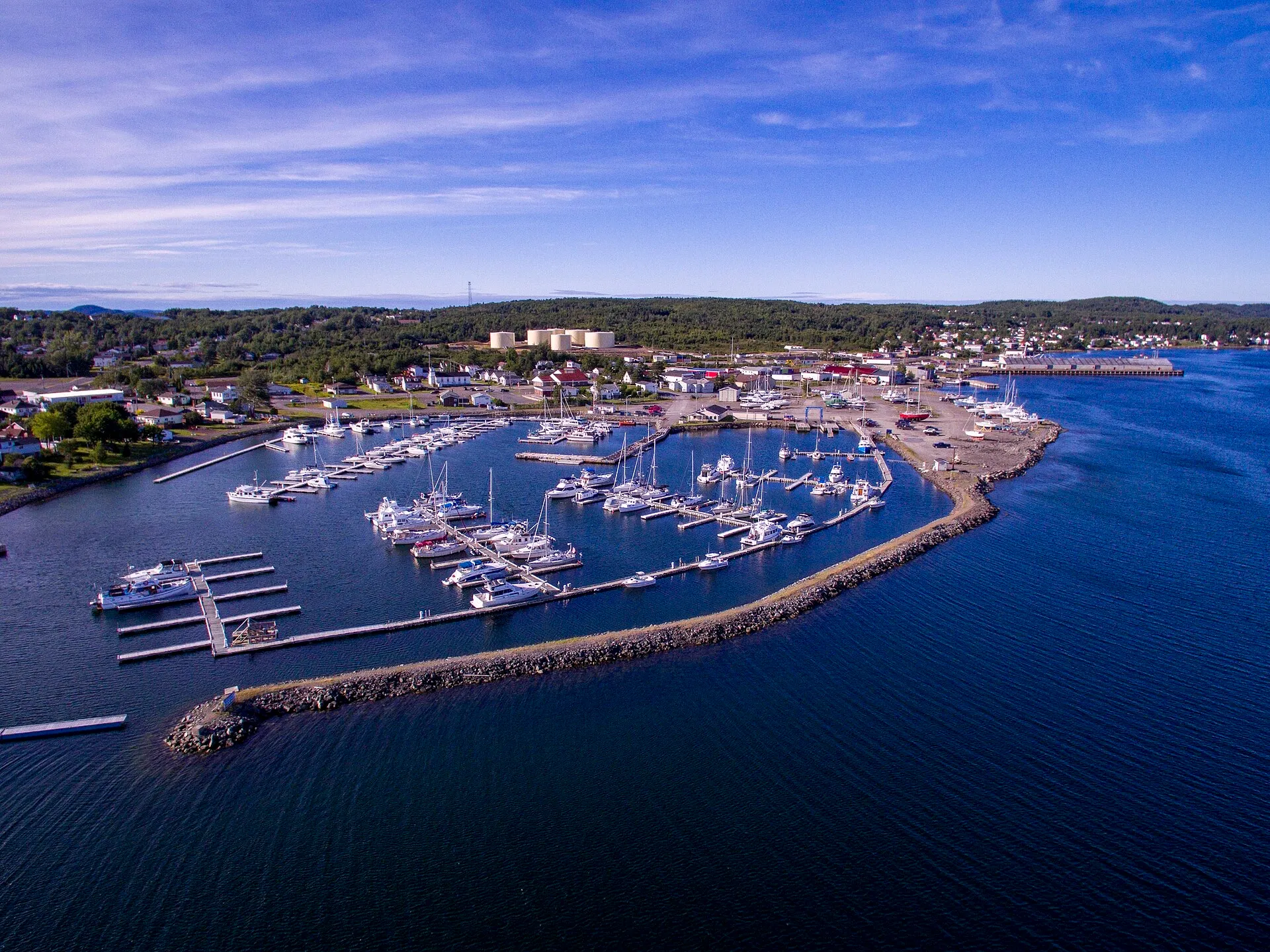 Lewisporte's marina from the air — breakwater, finger docks and sailboats, with the town spread along the shore of Burnt Bay behind.