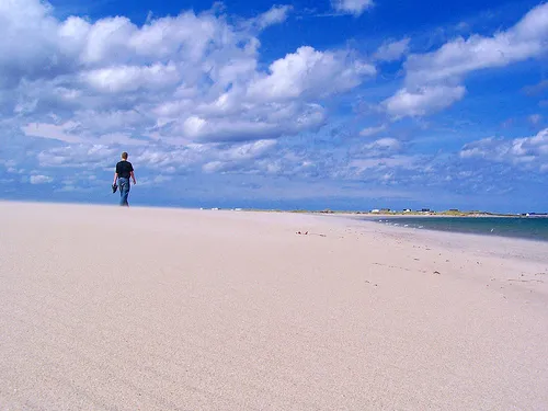 The sand at Lumsden on the Straight Shore — white beach running to the horizon under a big sky, one walker barefoot on it.