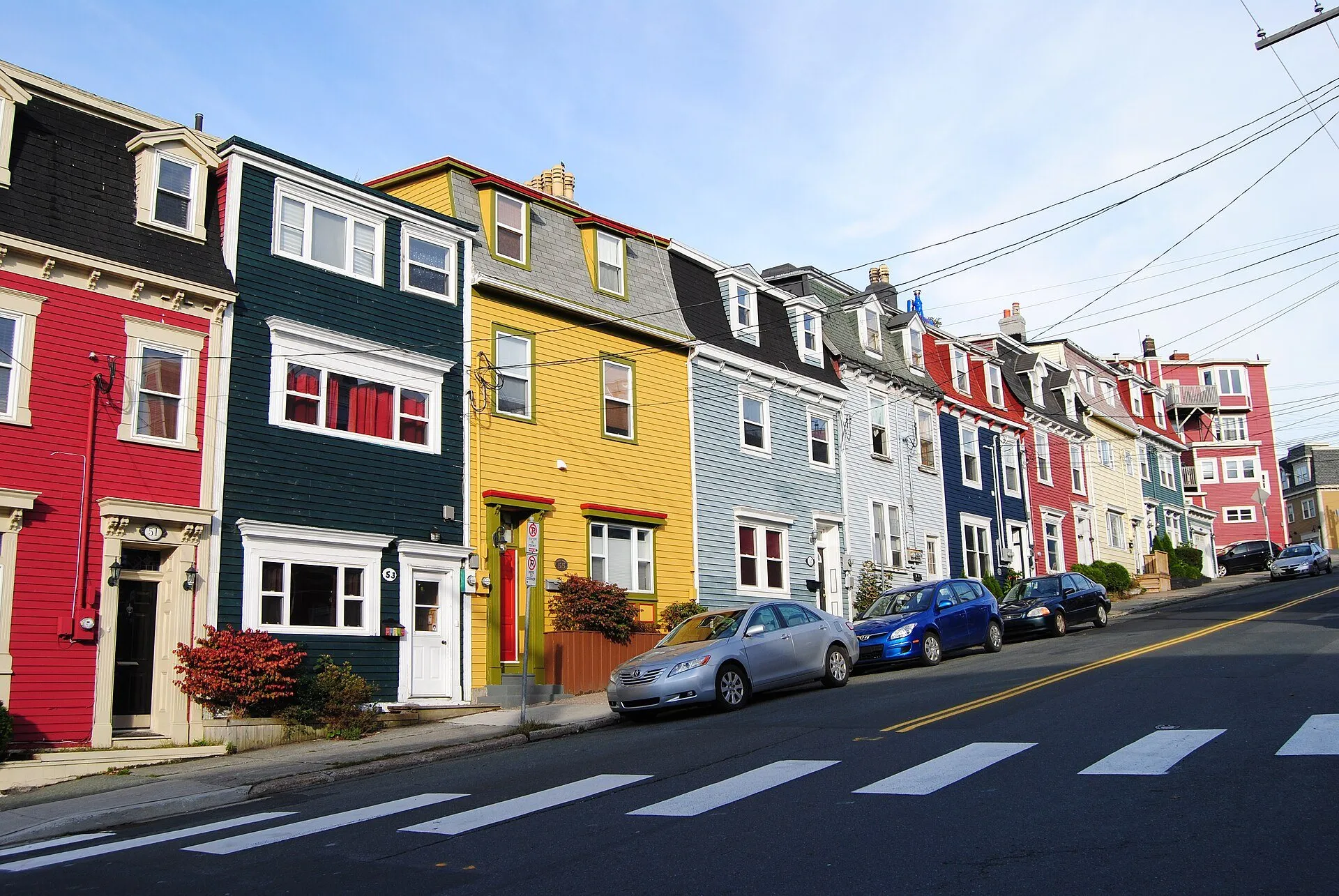 A row of brightly painted wooden row houses in red, green, yellow and blue climbing a street in downtown St. John's.
