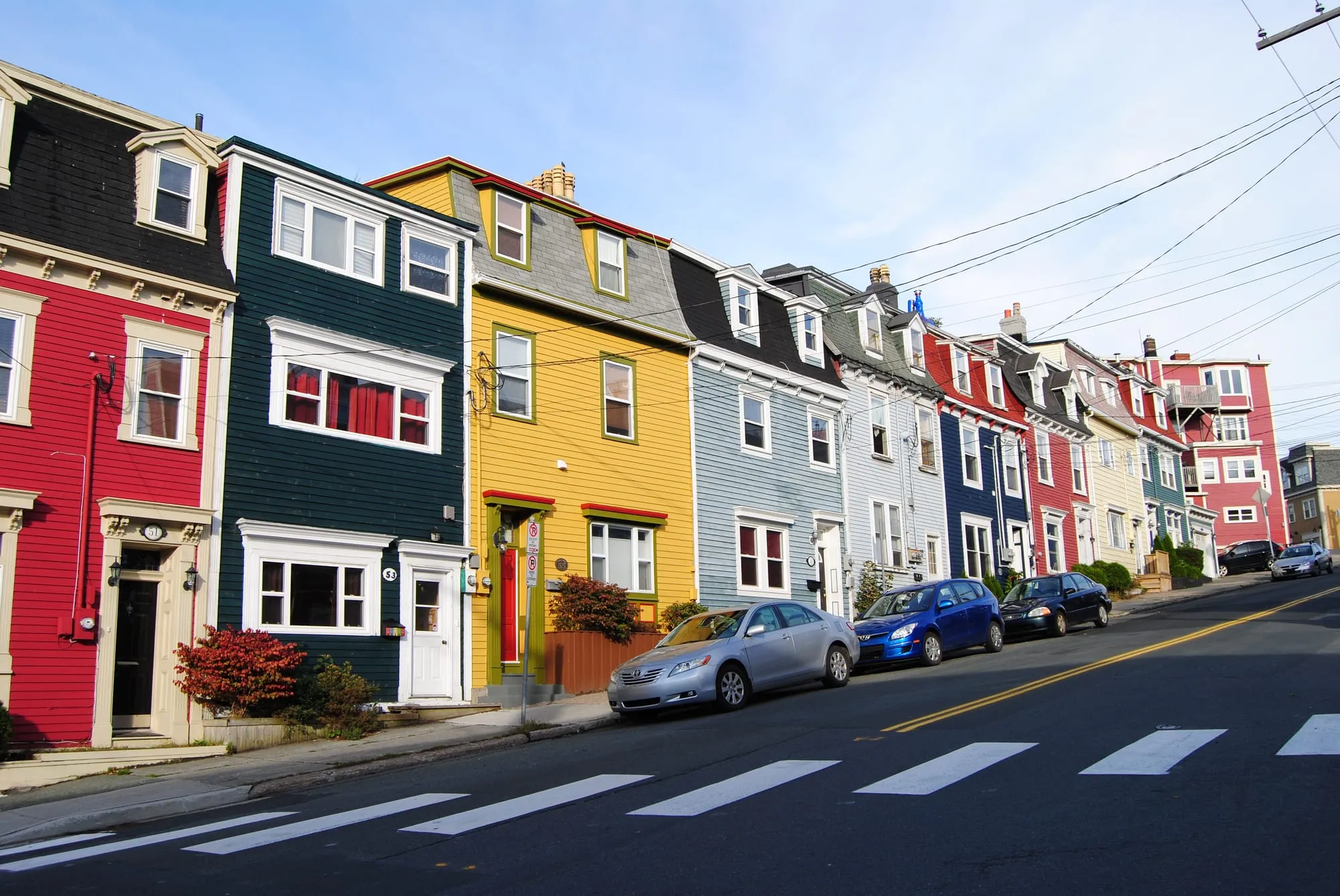 Downtown St. John's row houses painted red, green, yellow and blue, climbing a steep street under a blue sky.