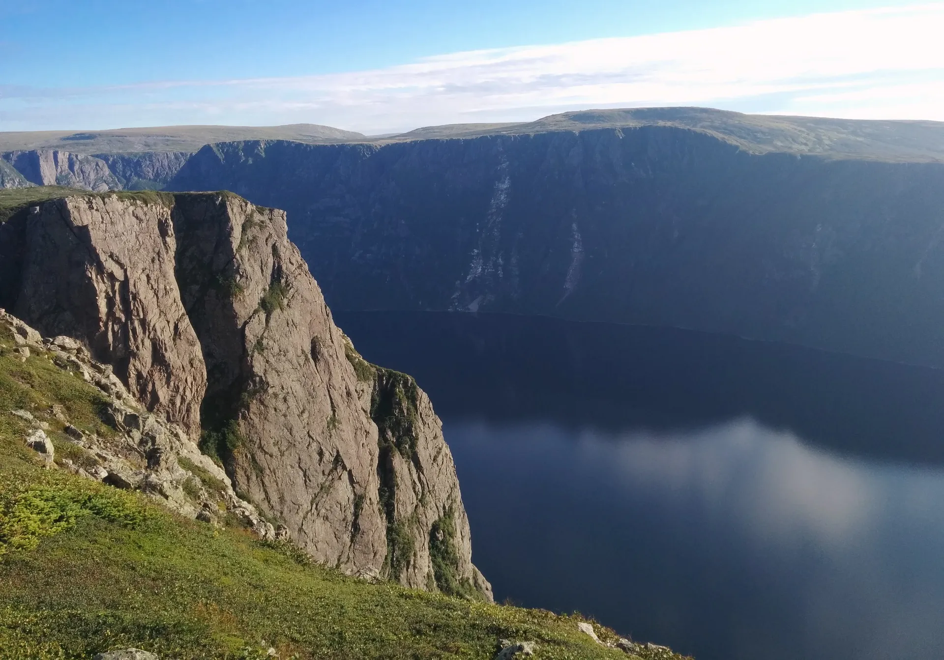 The rim of Western Brook Pond gorge in Gros Morne National Park — sheer rock walls dropping to dark water far below, the fjord running inland between the plateaus.
