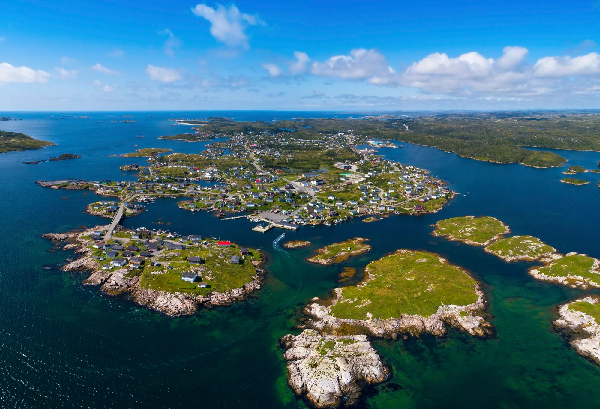Aerial of Burgeo spread across its rocky islands and causeways, deep blue water, bright day.