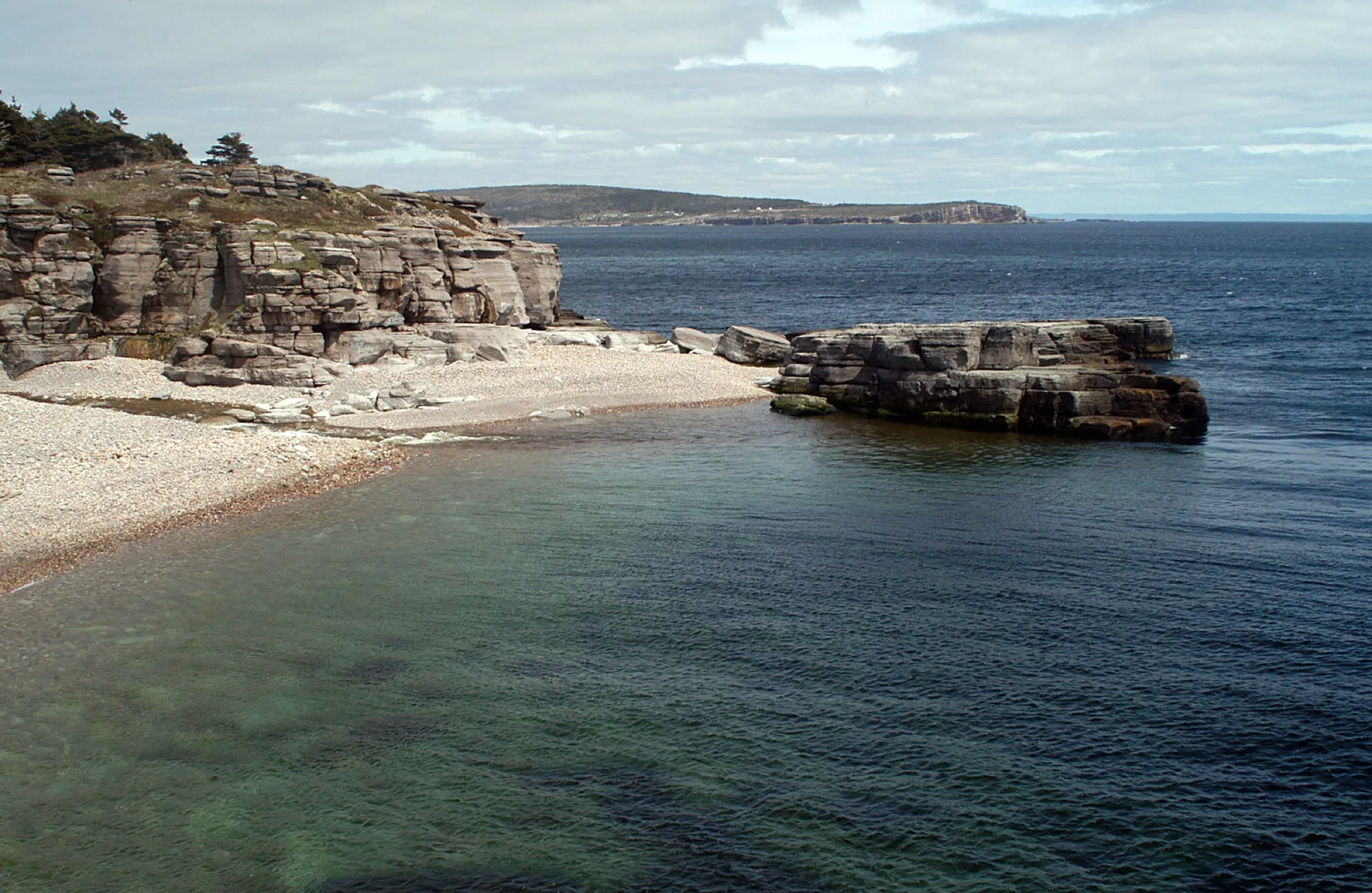 Limestone cliffs, a pebble cove and clear green water at Cape St. George, coastline running off behind.
