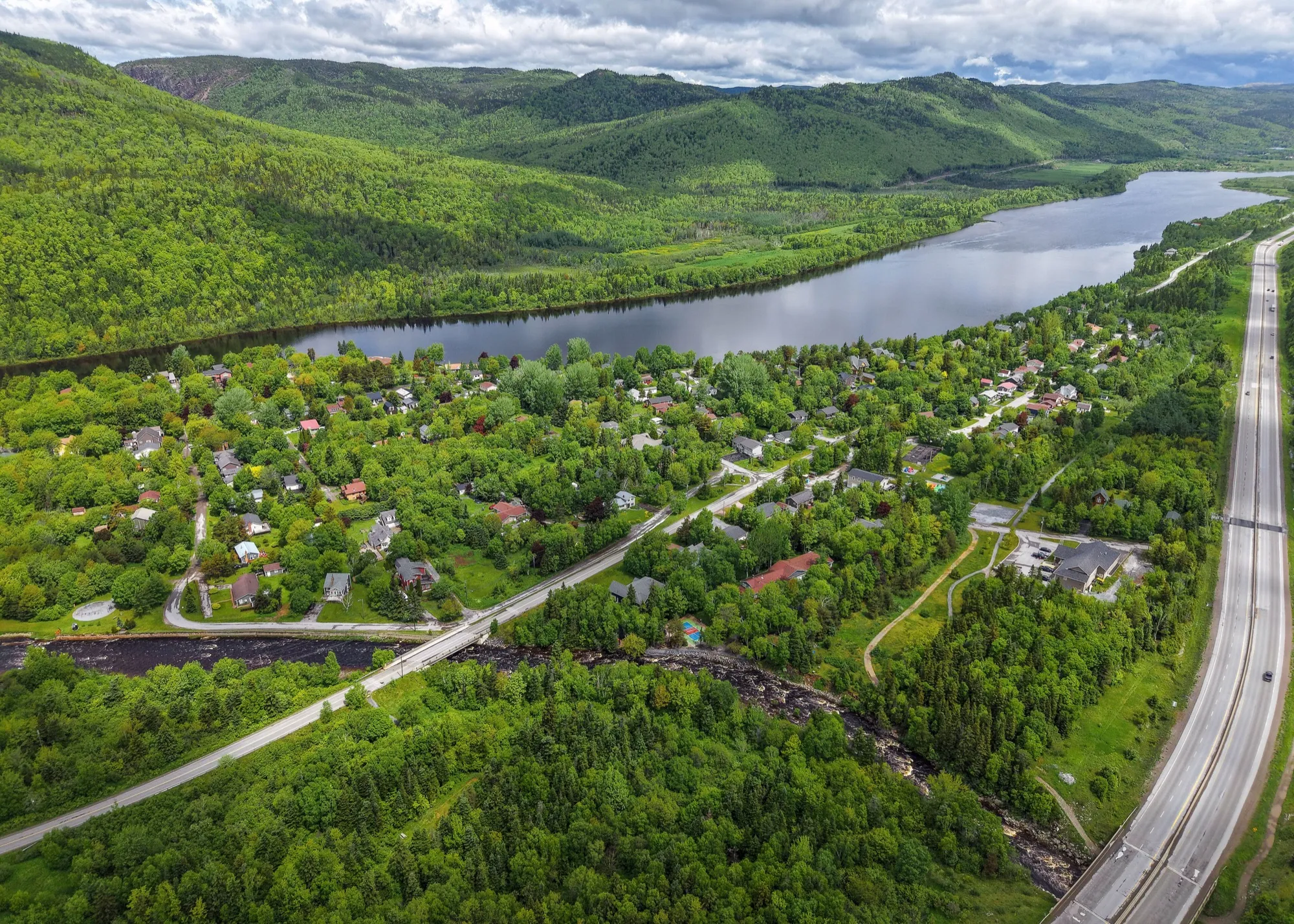 Aerial of Steady Brook and the Humber River in green summer, the Trans-Canada and the wooded valley sides - the base-lodge village.