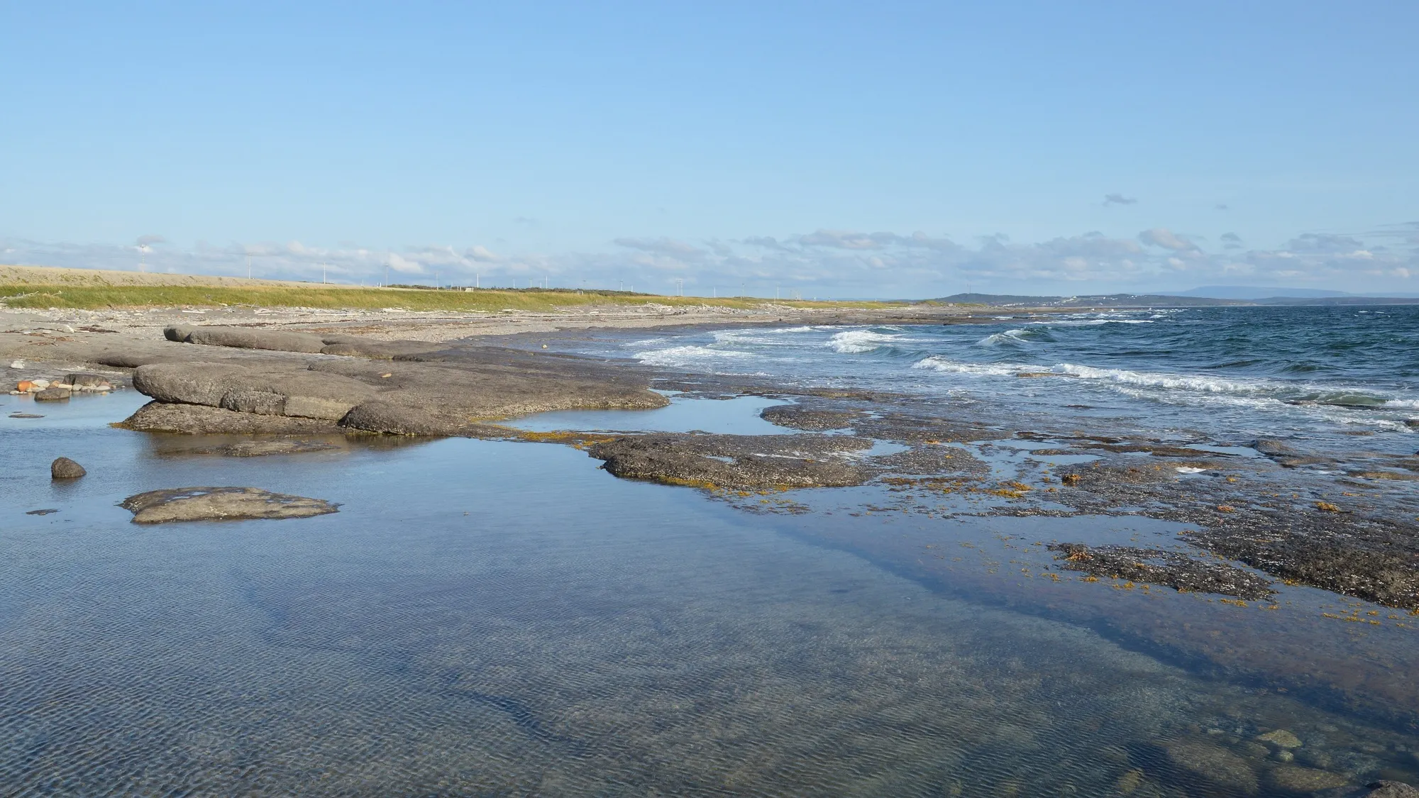 Limestone shore and tidal pools on Ingornachoix Bay at Port au Choix, bright blue-sky day.