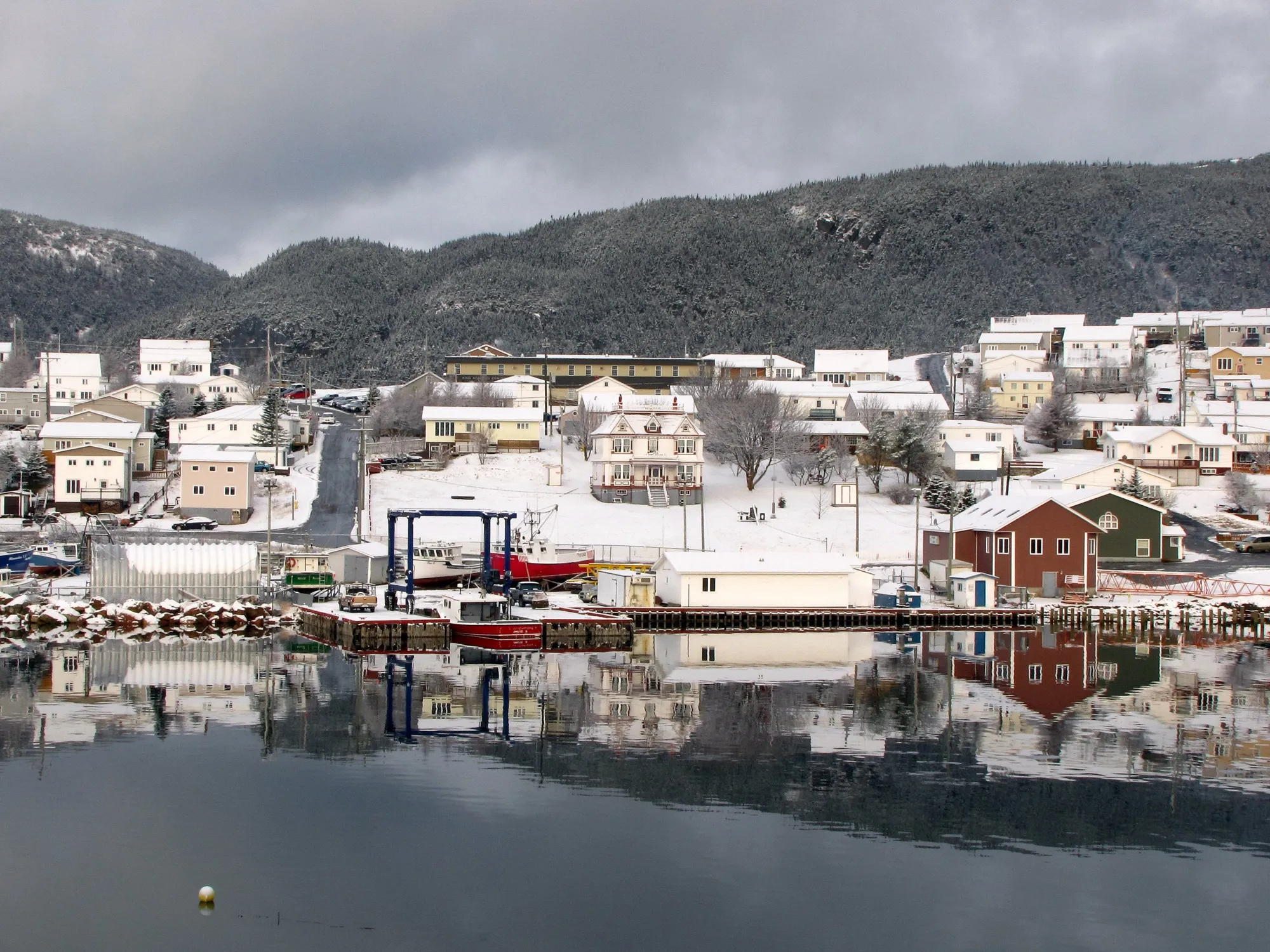 Harbour Breton waterfront and hillside houses reflected in the harbour, light snow, overcast.