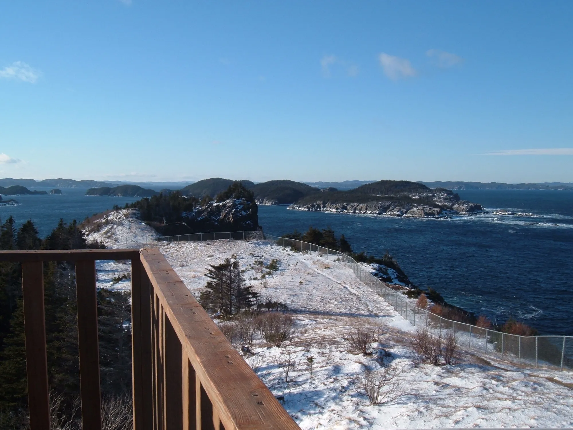 View from the Leading Tickles lookout over islands and open water, clear blue sky, light snow.